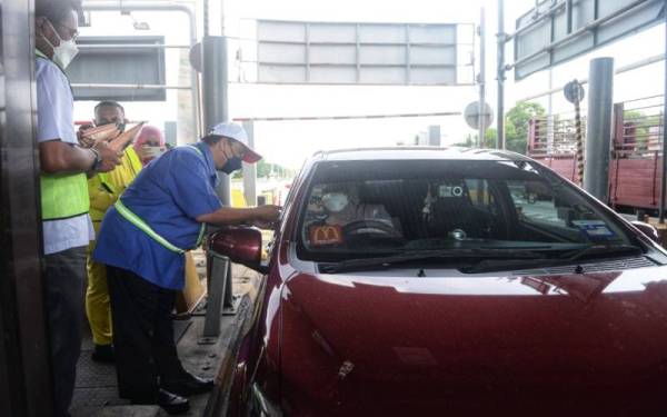 Che Had (dua dari kiri) mengedarkan cenderahati kepada pengguna lebuh raya di Plaza Tol Hutan Kampung di Alor Setar di sini pada Selasa.