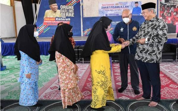 Annuar (kanan) menyampaikan sumbangan zakat kepada sebahagian pelajar pada Majlis Penyampaian Zakat Fisabilillah Pelajar Tingkatan 6 Atas dan 6 Bawah Parlimen Ketereh 2022 di Kompleks Yayasan Kemiskinan Kelantan (YKK), Melor pada Khamis. - Foto Bernama 