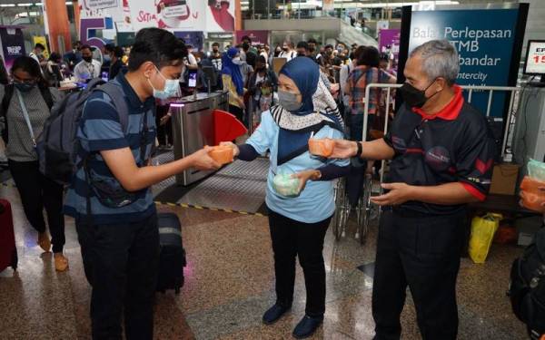 Rozita (tengah) bersama Mohd Zain (kanan) mengagihkan bubur lambuk kepada penumpang ETS di Stesen KL Sentral, Kuala Lumpur pada Rabu.