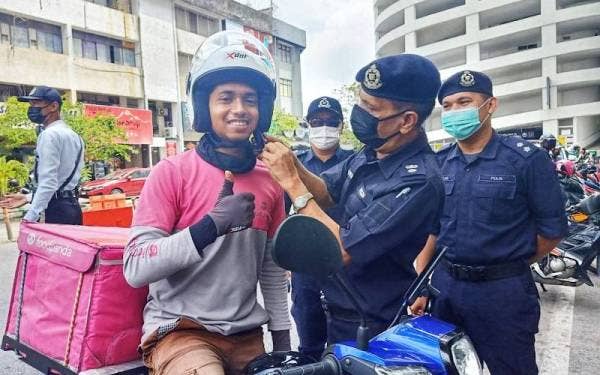 Mohd Mahiri memakaikan topi keledar kepada penunggang p-hailing di pekarangan Aman Central di sini pada Sabtu.