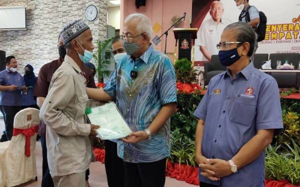 Mahdzir (tengah) menyerahkan geran hak milik rumah PPRT Keda kepada seorang penerima di SMK Pokok Sena, Pokok Sena pada Selasa.