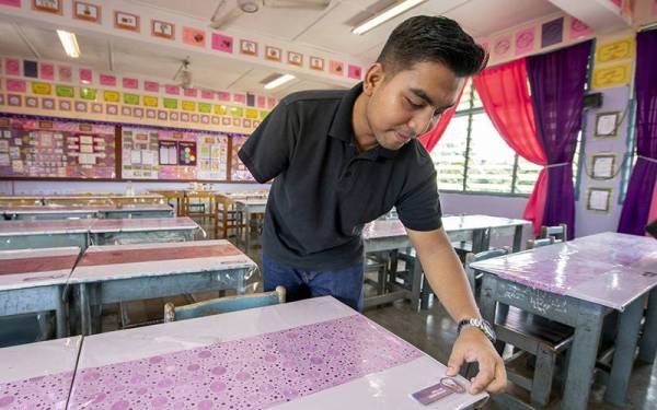 Abdullah menunjukkan gambar dan nama murid yang ditampalkan di setiap meja di kelasnya ketika ditemui di SK Tok Uban di sini baru-baru ini. - Foto Bernama