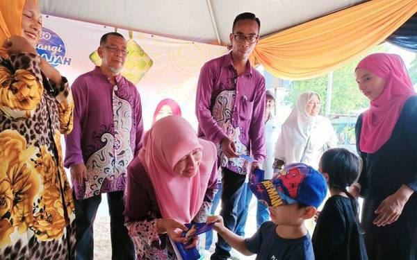 Wan Norashikin menyampaikan duit raya kepada kanak-kanak yang hadir ke Majlis Jamuan Hari Raya Aidilfitri di Pusat Khidmat DUN Kampung Gajah pada Khamis.
