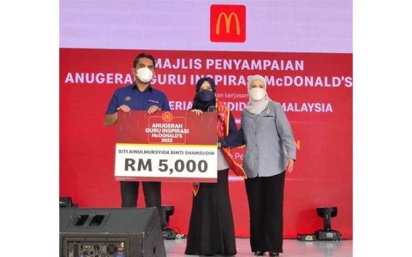 Mohd Radzi (kiri) menyampaikan Anugerah Guru Inspirasi McDonald’s 2022 kepada guru, Siti Ainulmursyida Shamsudin (tengah).
