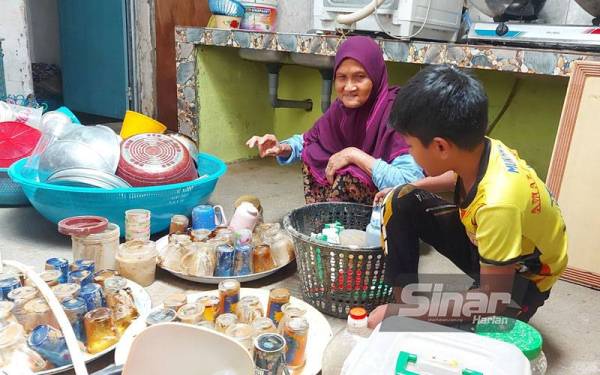 Saayah Nayan, 78, bersama cucunya menyusun pinggan mangkuk yang kotor selepas rumah dinaiki air di Felda Trolak Selatan.
