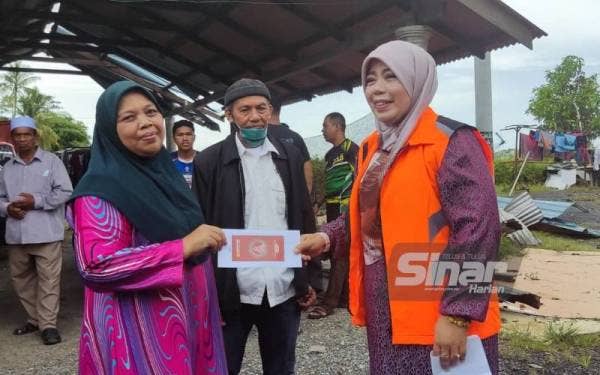Halimaton Shaadiah (kanan) menyampaikan sumbangan segera kepada seorang mangsa ribut di di Kampung Telaga Batu, Jitra pada Isnin.