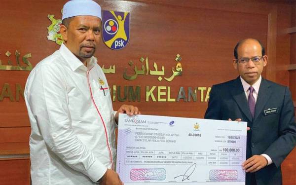 Wan Roslan (kiri) menyampaikan cek sumbangan kepada Setiausaha Perbadanan Stadium Kelantan, Mohd Roshdi Ismail semasa turun padang meninjau kerja-kerja naik taraf Stadium Sultan Muhammad IV di Kota Bharu pada Isnin.