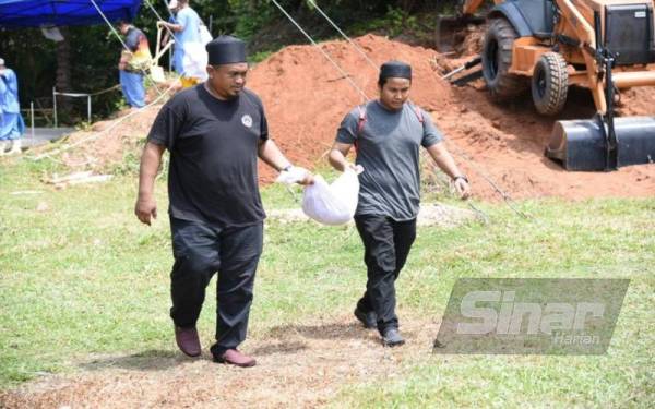 Dua individu membawa jenazah untuk dipindahkan dan dikebumikan semula di Tanah Perkuburan Islam Kampung Aur, Bukit Ibam di sini.