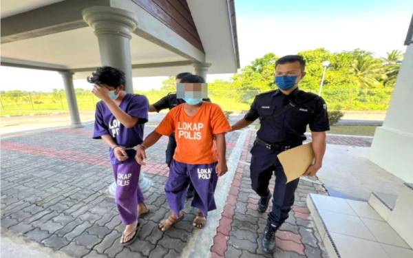 Tertuduh (tengah) dikawal polis ketika dibawa ke Mahkamah Pasir Mas pada Isnin