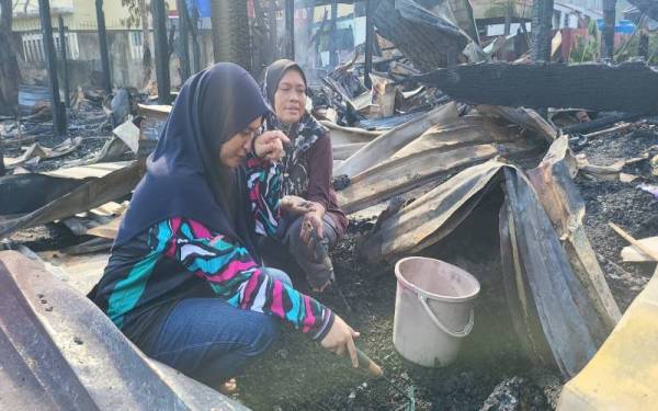 Hasrani (à droite) avec son fils sont sur le site de l'incendie à la recherche des économies de son fils qui ont été brûlées lors d'un incendie à Kampung Contoh, Petagas, Putatan.