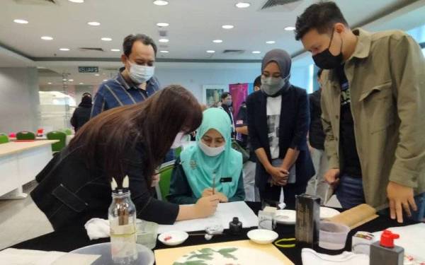 Alina (dua kanan) mengiringi Suzliana (duduk, tengah) melawat ruang pameran di program berkenaan.