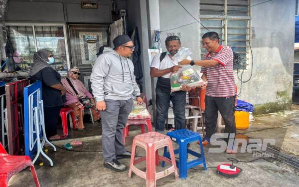 Norehan (kiri) melihat suaminya, Nizam (tiga dari kiri) menerima sumbangan makanan daripada ahli PSBM di Taman Limbongan Permai, pada Jumaat.