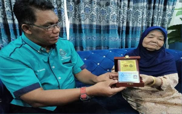 Baharudin (kiri) melihat plak penghargaan yang diterima pesara polis zaman darurat, Zainab Wan Mohamed dalam kunjungan kasih Persatuan Bekas Polis Malaysia(PBPM) Wilayah Persekutuan di Meru di sini, pada Sabtu.