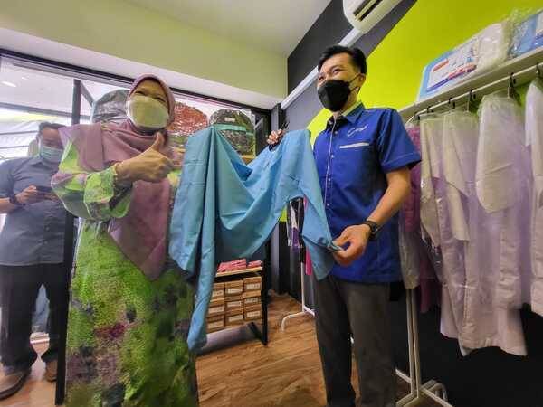 A Safuan menunjukkan pakaian seragam sekolah kepada Azizah bahawa ia jenis berkualiti tinggi dan dijual dengan harga yang berpatutan sesuai untuk golongan B40.