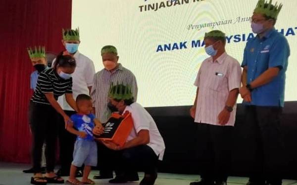 Khairy Jamaluddin (duduk) menyampaikan sumbangan kepada anak-anak Orang Asli pada Majlis Perasmian dan Pelancaran Tinjauan Kesihatan Orang Asli di Dewan Komuniti Sahom pada Sabtu.