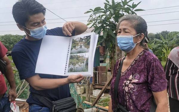 Seng Hoo (dua dari kiri) bersama anaknya menunjukkan gambar beberapa batang pokok durian miliknya musnah didakwa berpunca daripada air kawasan pelupusan sampah mengalir ke kebunnya.
