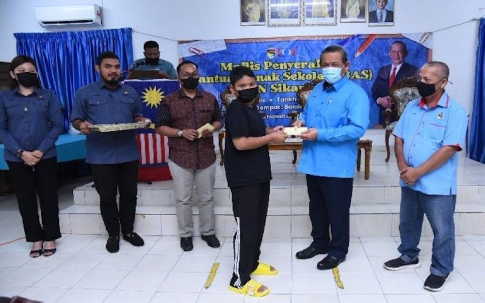 Aminuddin (dua kanan) menyampaikan bantuan kepada seorang pelajar pada Majlis Penyerahan Bantuan Anak Sekolah DUN Sikamat pada Khamis.