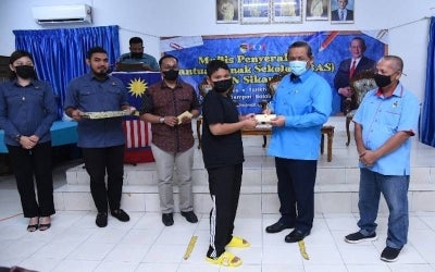 Aminuddin (dua kanan) menyampaikan bantuan kepada seorang pelajar pada Majlis Penyerahan Bantuan Anak Sekolah DUN Sikamat pada Khamis.