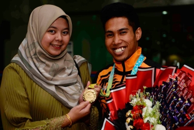 Wira Negara Muhammad Aznil Bidin yang merupakan pemenang pingat emas (rekod baharu) angkat berat Sukan Komanwel 2022 bersama isterinya Aina Izzati Masri, 23, ketika tiba di Lapangan Terbang Kepala Batas, pada Ahad. - Foto Bernama
