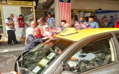 Kalsom (kiri) melekatkan Jalur Gemilang di pada sebuah teksi di Terminal Teksi Melaka Sentral, pada Selasa.