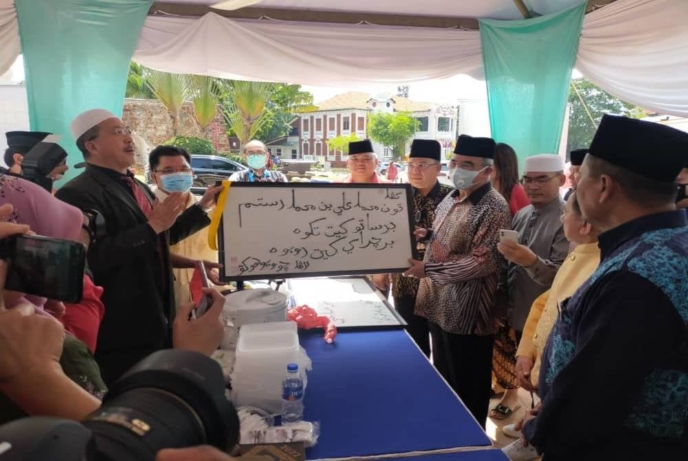 Liu Bao Jun (kiri) menunjukkan tulisan khat yang dihasilkan kepada Mohd Ali (dua dari kanan) di Balai Syed Sheikh Al-Hadi, Bastion House, Banda Hilir, pada Khamis.