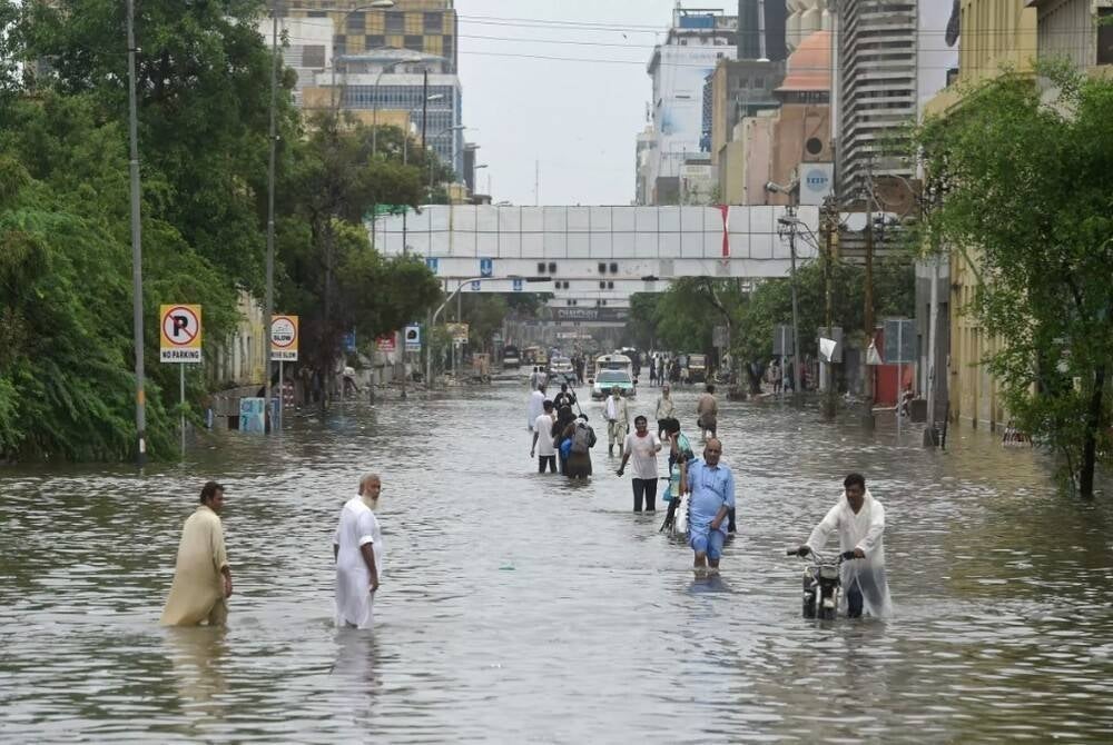 Orang ramai mengharungi jalan yang dinaiki air di Karachi. Foto AFP