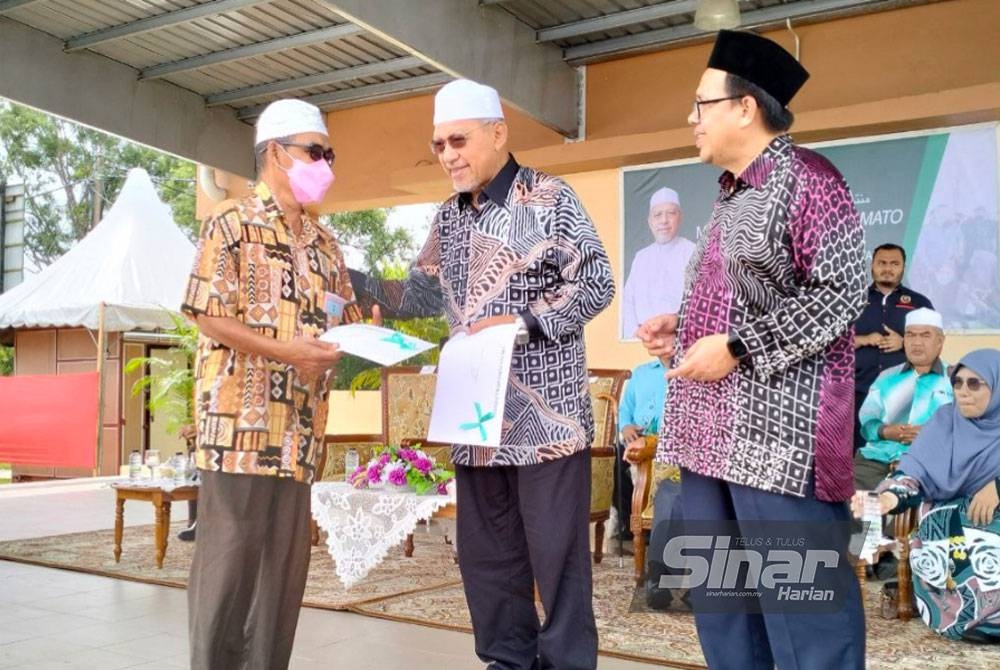 Ahmad (tengah) menyampaikan geran tanah kepada Nik Rahim (kiri) pada Program Jjupo Mata Menteri Besar dan pemimpin bersama rakyat di Dataran Bandar Baru Pasir Mas pada Khamis.