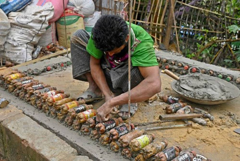 Seorang pelarian Rohingya membina dinding pondok menggunakan botol kosong sebagai ganti batu bata.