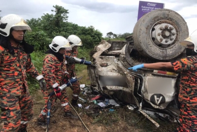 Pasukan bomba berusaha mengeluarkan mangsa yang tersepit dari treler terbalik di lebuh raya dekat Tanjung Malim. Foto: Ihsan bomba