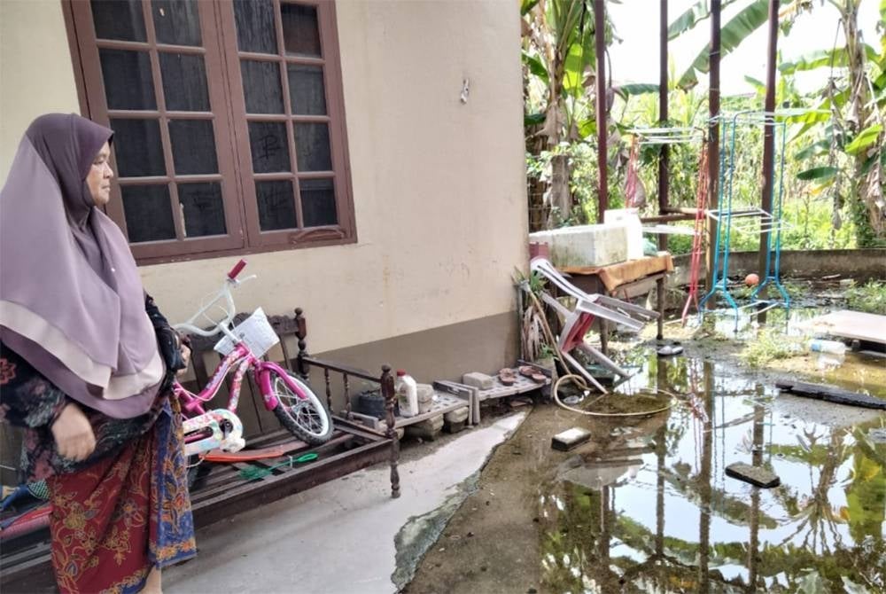 Hamidah melihat banjir termenung di belakang rumahnya.