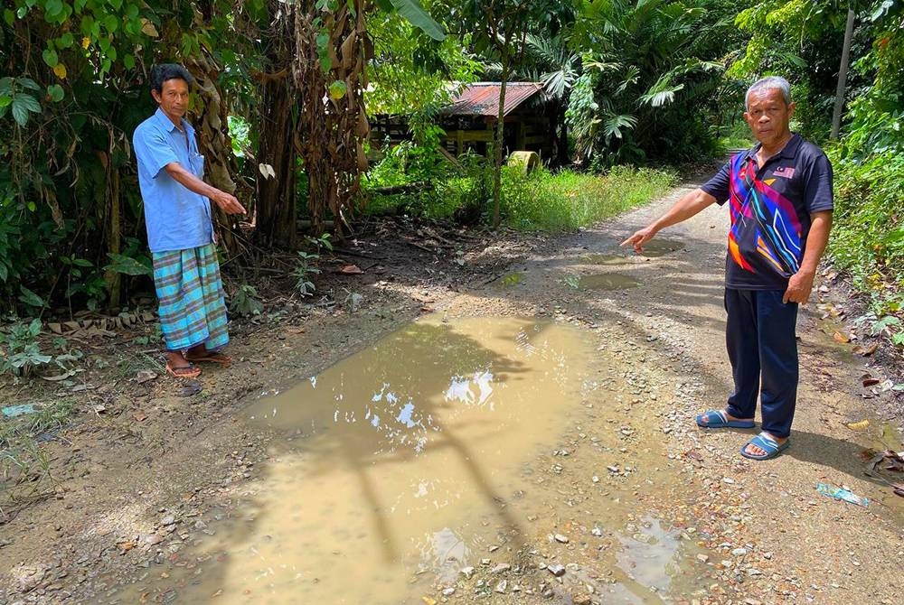 Zakaria (kanan) dan Nazri menunjukkan keadaan jalan yang becak dan berlopak sekali gus mengundang bahaya kepada penduduk.