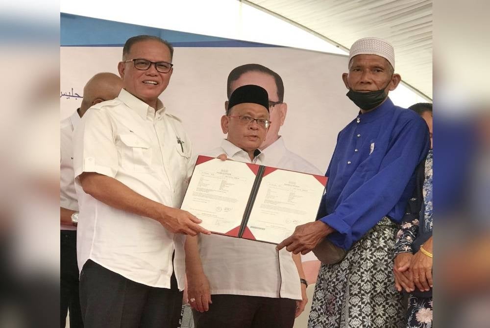 Wan Rosdy (kiri) menyampaikan geran hak milik tanah kepada salah seorang peneroka pada majlis penyerahan surat hak milik tanah Felda, hak milik Felcra dan notis 5A kepada peneroka di Dewan Felda Bukit Sagu 1 di sini pada Ahad.