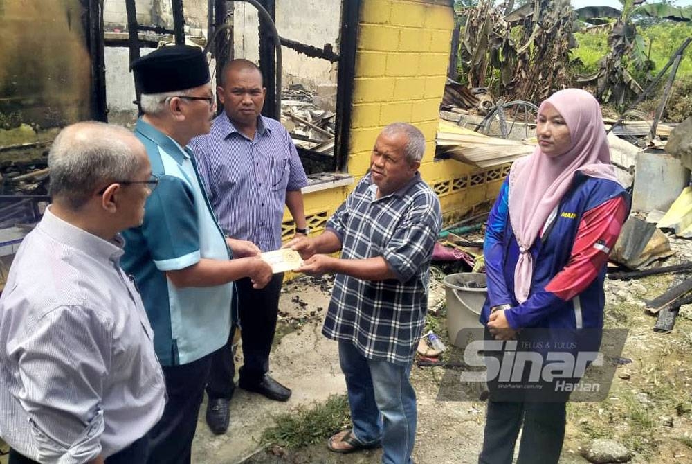 Md Rawi (dua dari kiri) menyampaikan sumbangan wang tunai kepada mangsa rumah terbakar, Ibrahim Kadir (empat dari kiri) di Kampung Belimbing Dalam di sini, pada Rabu.