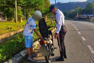 Anggota polis melakukan pemeriksaan terhadap seorang penunggang motosikal dalam operasi terbabit. -Foto PDRM