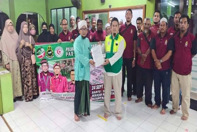 Rosli (kiri) menerima borang pendaftaran Sukarelawan Banjir Pas Kuantan diserahkan Saharudin di Masjid Al Fatah, Batu 3 di sini pada malam Sabtu.