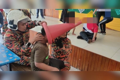 Anggota bomba berusaha mengeluarkan kepala seorang murid lelaki yang tersangkut kon di sebuah sekolah di Pontian pada Selasa. - Foto Ihsan Bomba