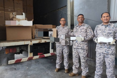 Siva Kumar (tengah) menunjukkan antara rokok seludup yang dirampas di persisiran pantai Batu Laut, Banting pada Rabu.