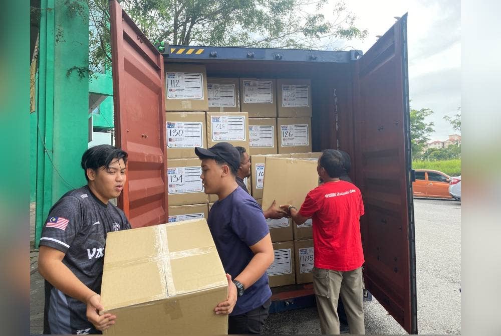 Sukarelawan menyusun kotak pakaian ke dalam kontena di Laman 83, Bukit Jelutong pada Ahad.
