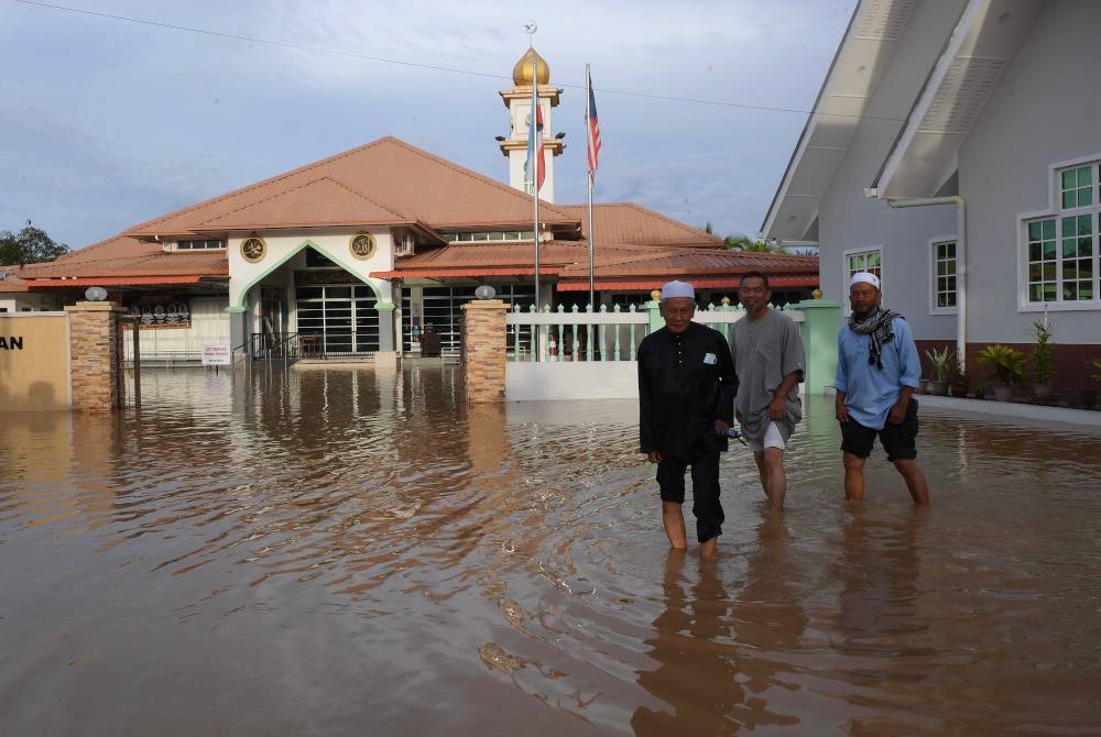 Tiga orang penduduk Kampung Ketiau meredah banjir ketika menunaikan solat di Masjid Kampung Ketiau, Kota Kinabalu. - Foto Bernama