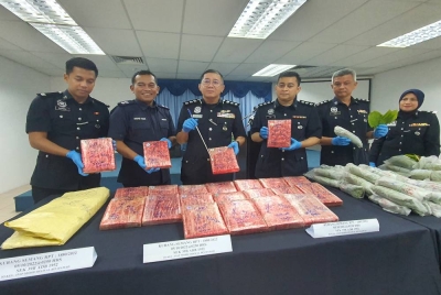 Cheng San (tiga dari kiri) bersama pegawai penyiasat kes menunjukkan ketulan ganja yang dirampas daripada pasangan suami isteri dalam serbuan di Taman Malwira, Kubang Semang pada Rabu lalu.