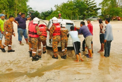 Anggota bomba dan orang awam menolak Perodua Myvi yang tersangkut di pesisir Pantai Sentosa pada Rabu.