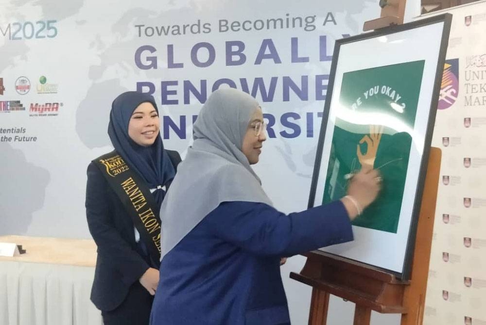 Roziah diiringi Rita Sosilawati menandatangani poster 'Are You Ok Centre' di UiTM Shah Alam pada Khamis.