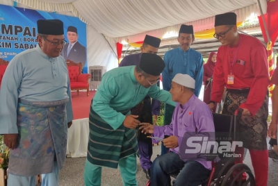 Amirudin (dua dari kiri) menyampaikan surat hak milik tanah kepada seorang penerima di pekarangan Masjid Jamek Sultan Hisamuddin pada Jumaat.