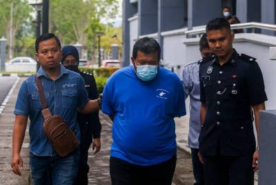 Tertuduh (tengah) diiring polis ketika tiba di mahkamah.