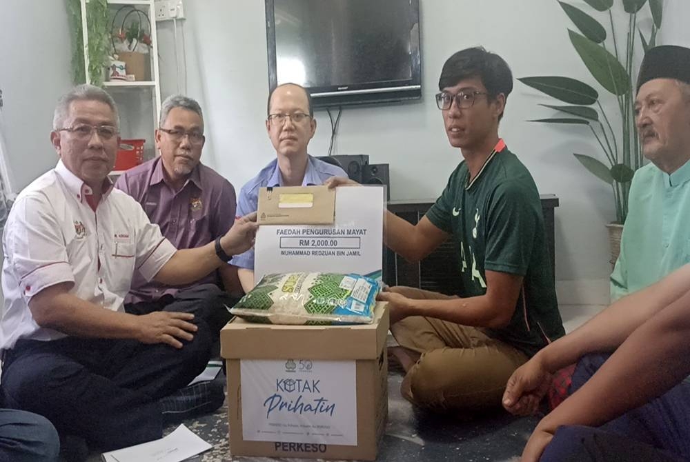 Adham (kanan) menyerahkan bayaran faedah Perkeso kepada Redzuan di rumahnya di Kampung Lukut Batu 4 pada Khamis.