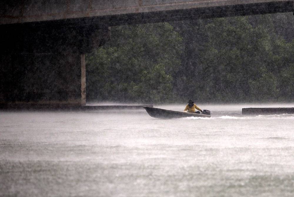 Seorang nelayan dilihat menyusuri sungai dengan sebuah bot kecil dalam keadaan hujan lebat berhampiran Jeti Nelayan Pengkalan Kempas. 