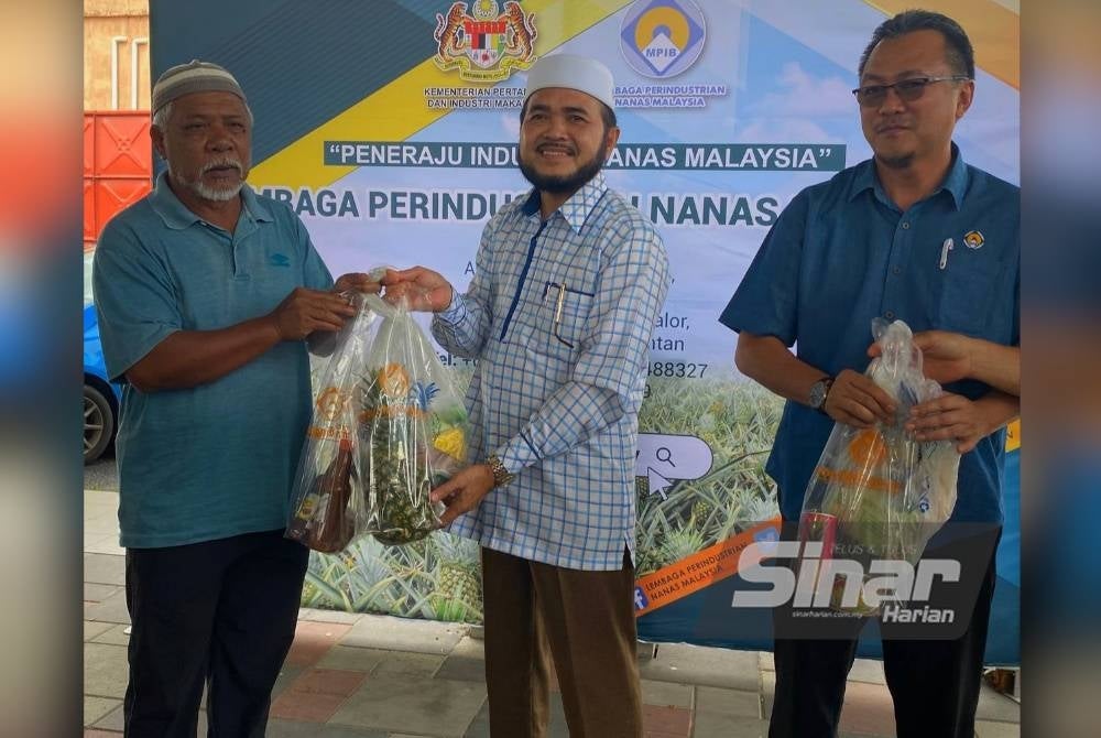 Nik Muhammad Zawawi (tengah) mengagihkan nanas percuma kepada penerima semasa program promosi makan buah nanas segar dan agihan ayam nanas LPNM Kelantan di Pasir Puteh pada Sabtu.