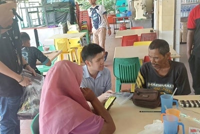Wei Jiet (tengah) mengedarkan pelitup muka di sekitar Pekan Nanas pada Ahad.