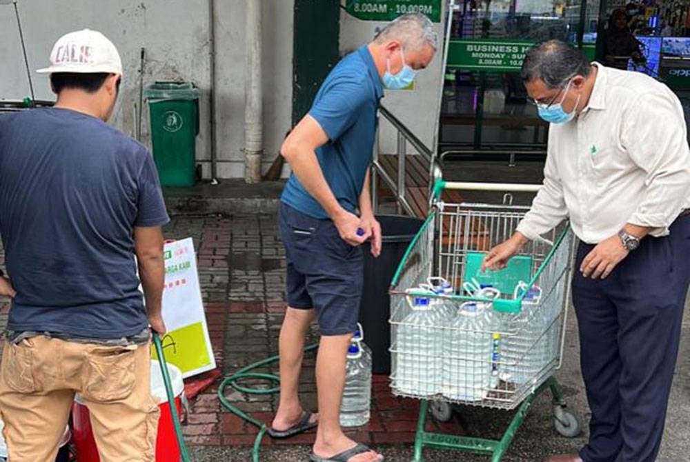 Mas Imran (kanan) membantu penduduk mengambil air percuma yang disediakan pihak Pasar Raya Econsave Permas Jaya, Johor Bahru pada Selasa