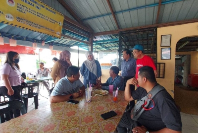 Fathin Amelina (kiri) dan Nurul Izzah bermesra dengan pelanggan di Kedai Ikan Bakar Sempadan di sini pada Khamis.